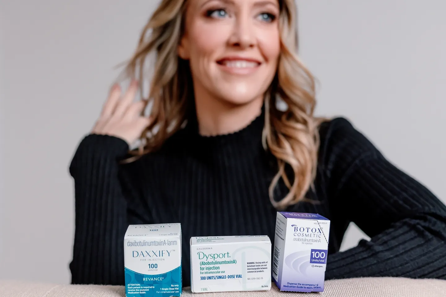 A woman sitting in front of three different types of skin care products.